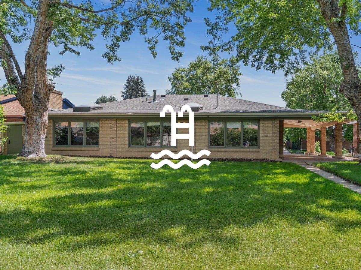 Single-story brick ranch home with a wide green lawn, mature shade trees and a covered patio