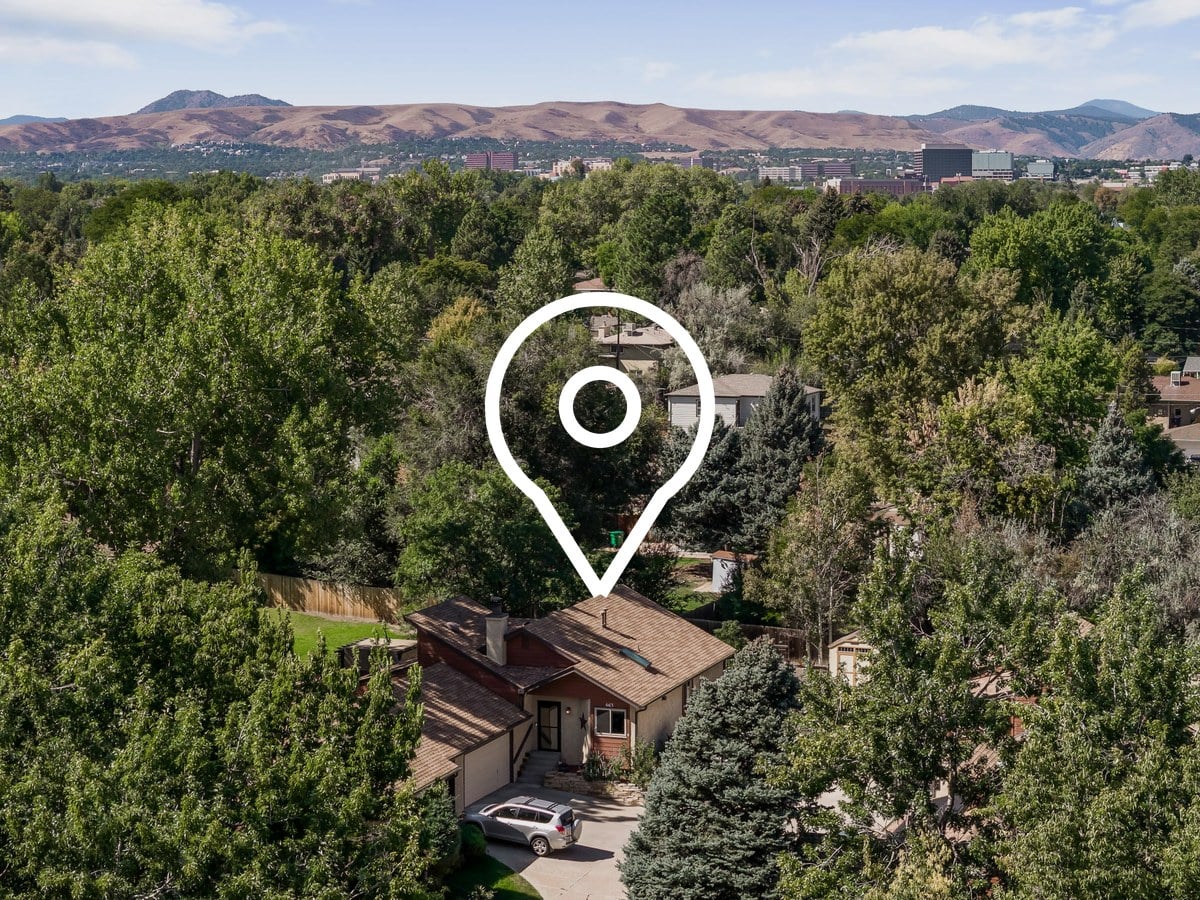 Aerial view over tree-covered suburban homes toward the foothills west of Denver