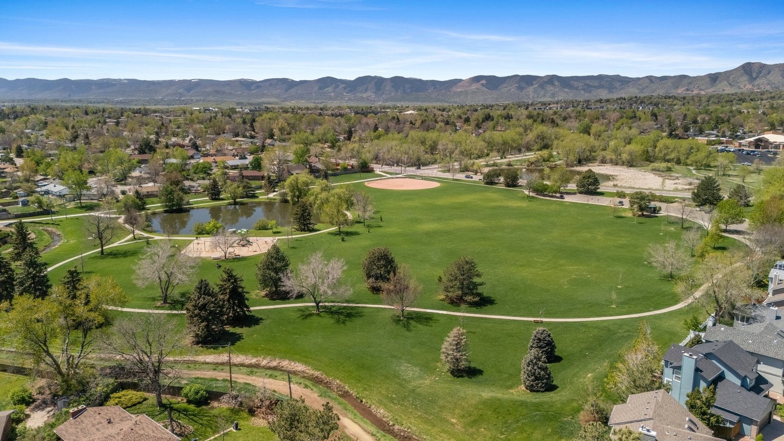 Aerial view of a Denver-area park with a loop path, pond and mountain views