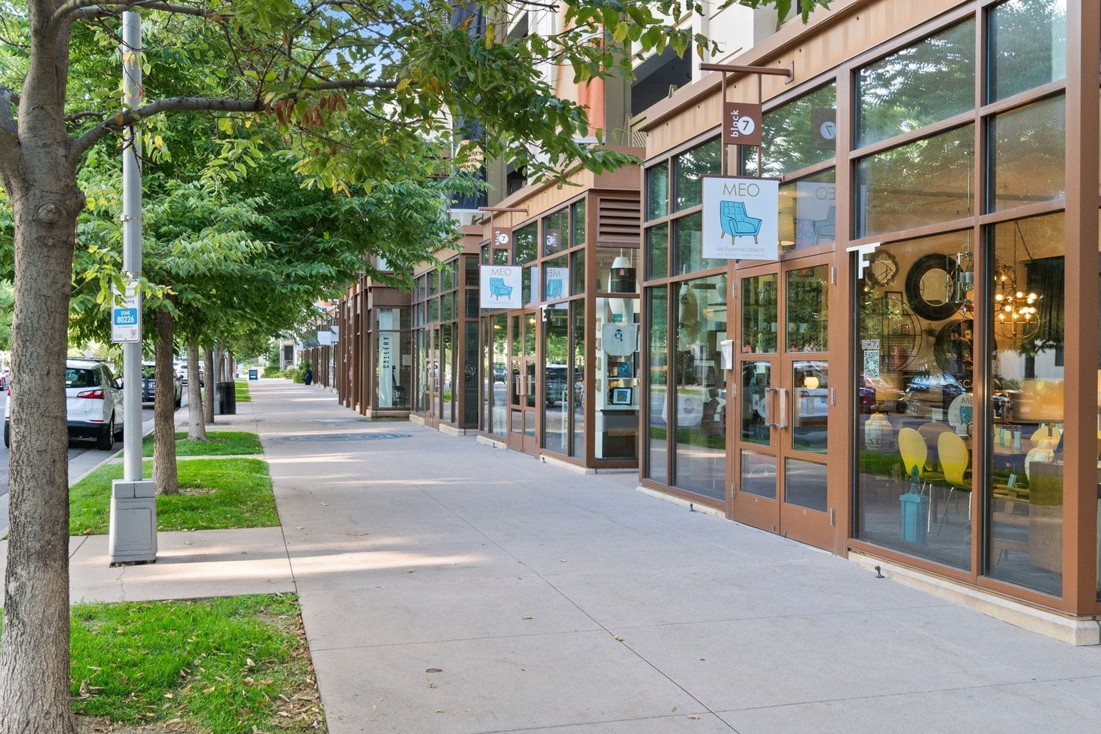 Ground-floor shops and a wide tree-lined sidewalk on a mixed-use Denver street