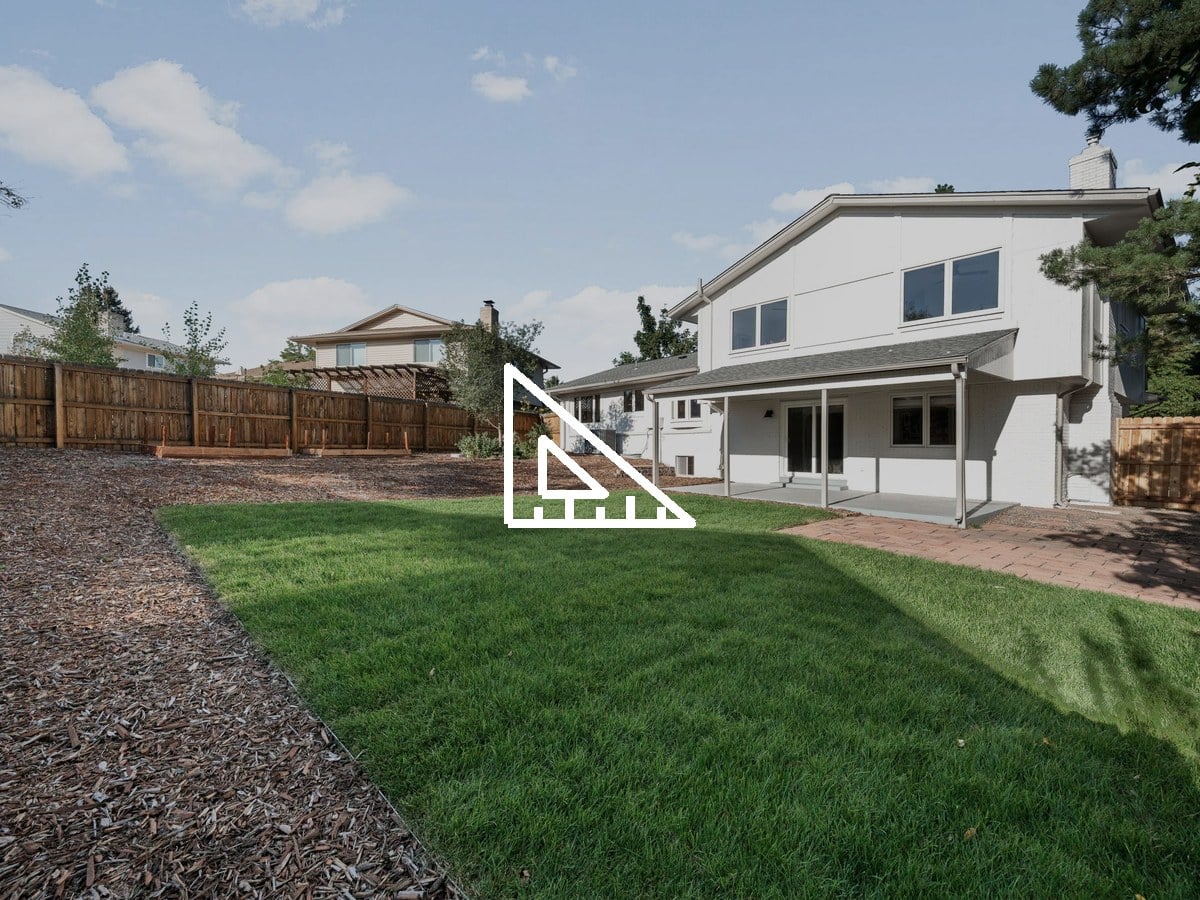 Fenced backyard with a lawn, mulch beds and a covered patio behind a two-story home