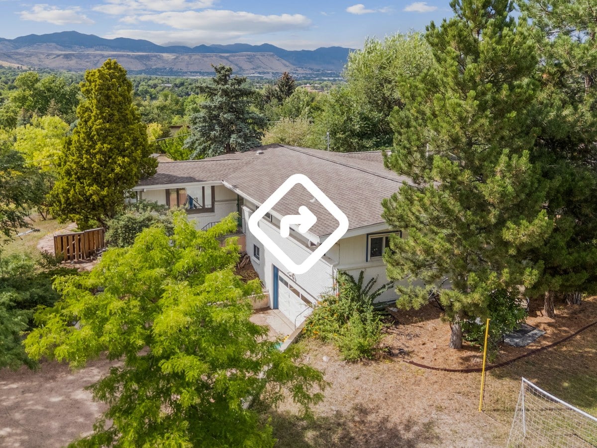 Aerial view of a ranch home among tall evergreens with the foothills in the distance