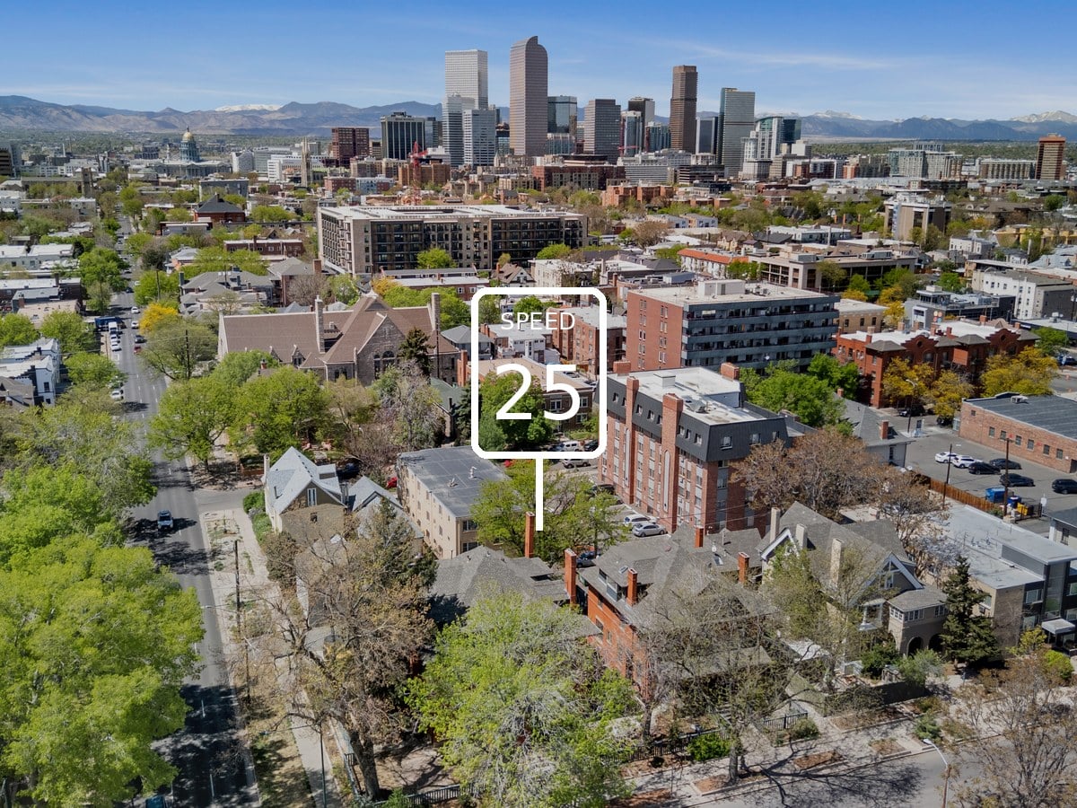 Aerial view of tree-lined streets, brick apartment buildings and houses with the downtown Denver skyline and mountains beyond