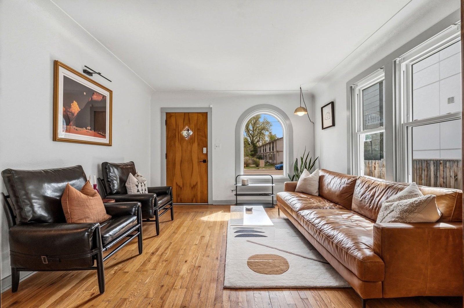 Living room with original hardwood floors, a wood front door and an arched window in an older Denver home