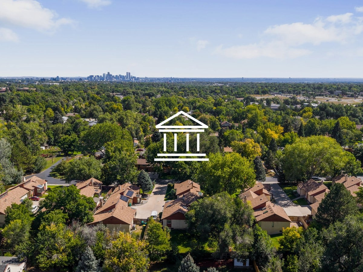 Aerial view of tree-lined residential streets and townhome rooftops with the downtown Denver skyline on the horizon