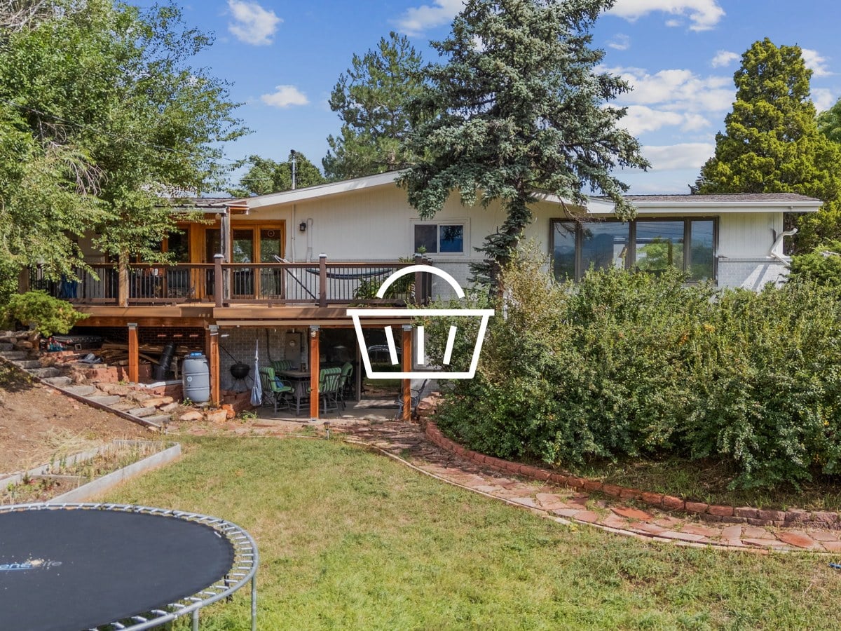 Rear view of a ranch home with a raised wood deck, covered patio, lawn and stone garden border