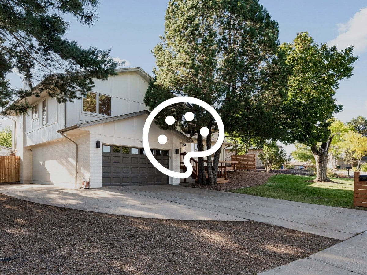 Two-story white brick home with a dark two-car garage door, pine trees and a curved concrete driveway