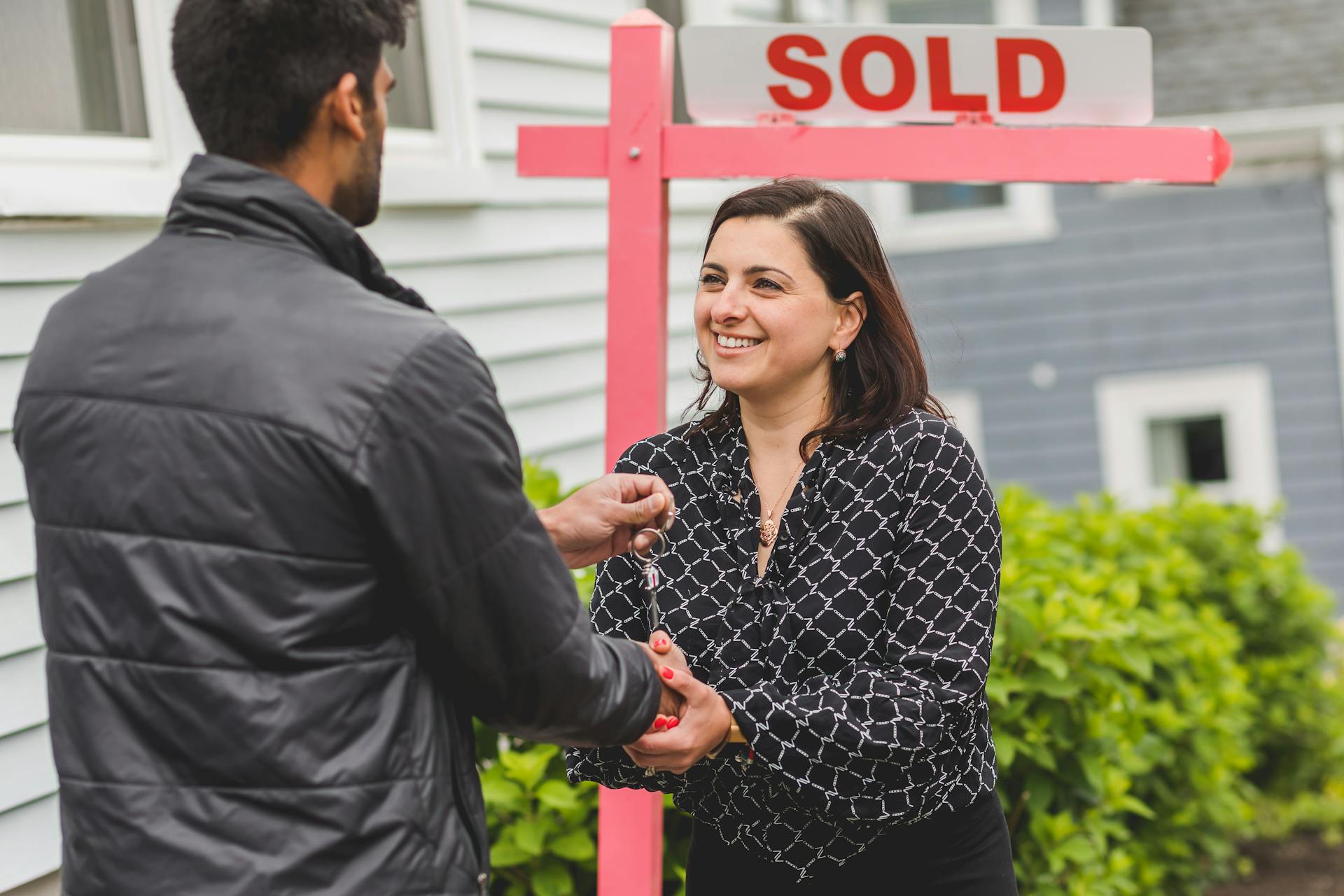 Smiling homeowner standing near a sold sign in front of a Boston house in June 2025, representing National Homeownership Month and strong local market activity.