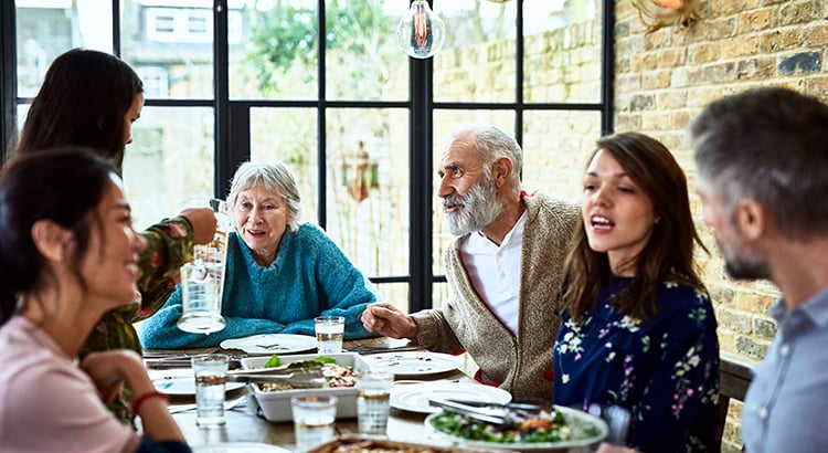 Extended family sitting round dinner table chatting and eating dinner