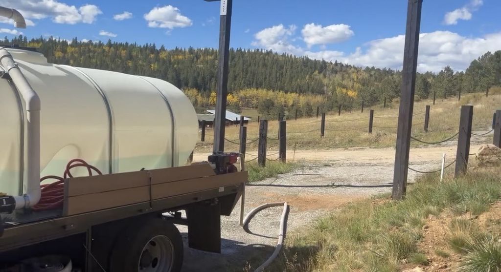 Water truck backed up to a cistern at a mountain home in Central City, Colorado, with the fill hose connected and aspens turning in the background