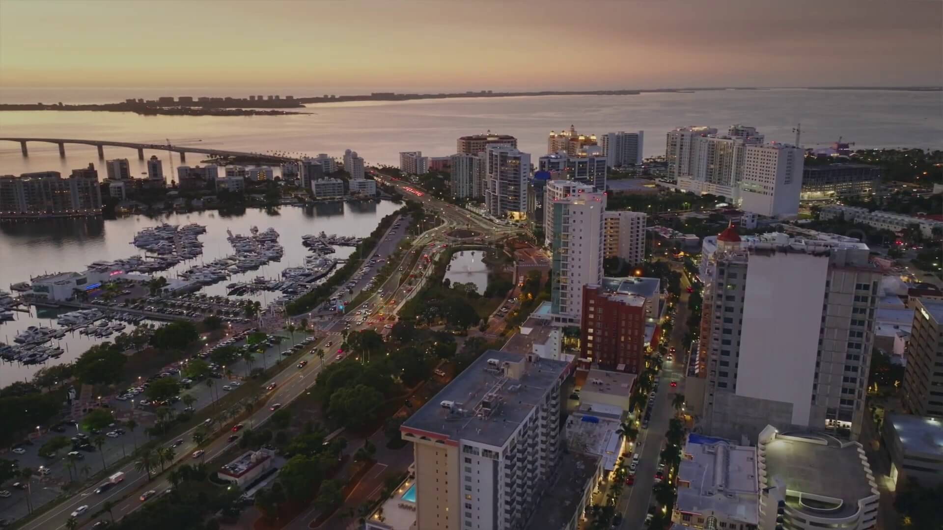 Aerial perspective of Sarasota during sunset, with the cityscape illuminated by warm, golden light.