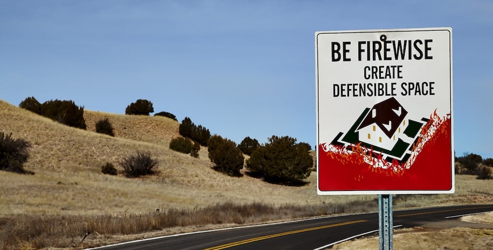 Firewise sign in Angel Fire, NM urging homeowners to create defensible space for wildfire protection and home insurance eligibility.