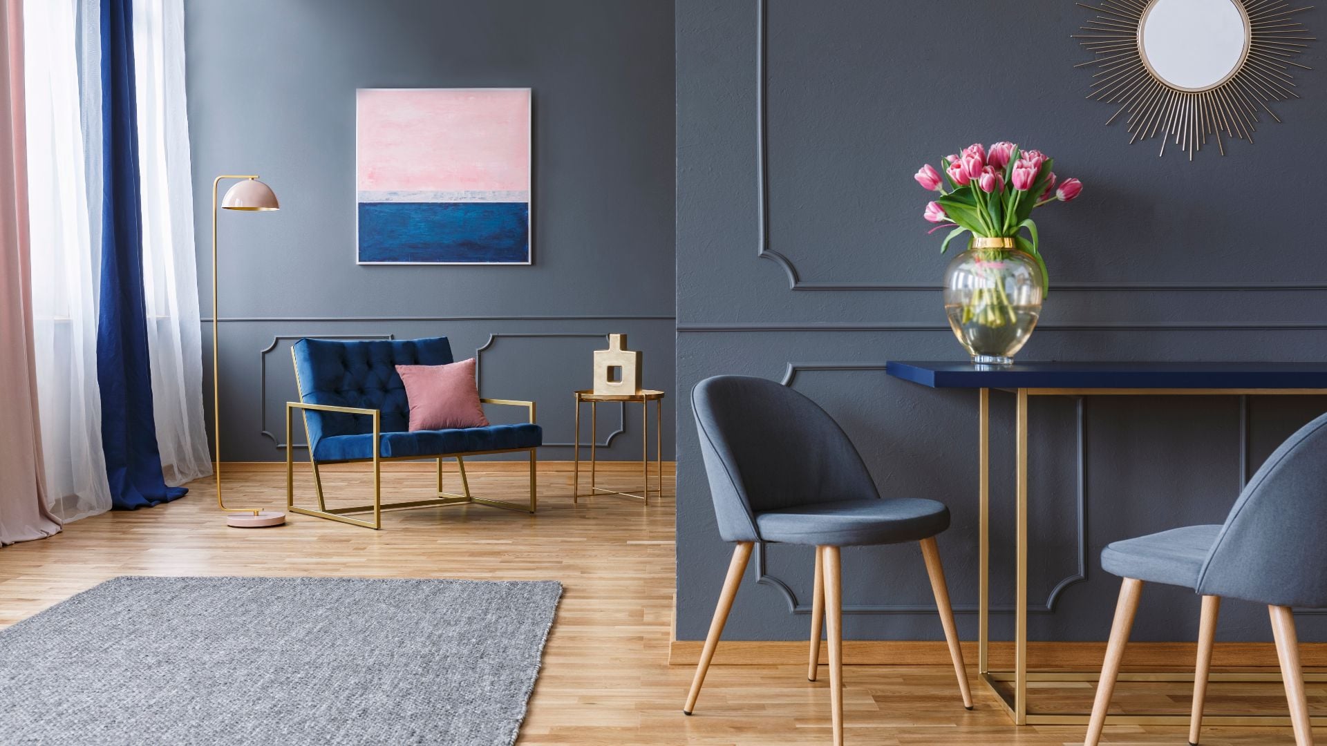 Pink flowers on table in grey elegant living room interior with gold mirror and painting