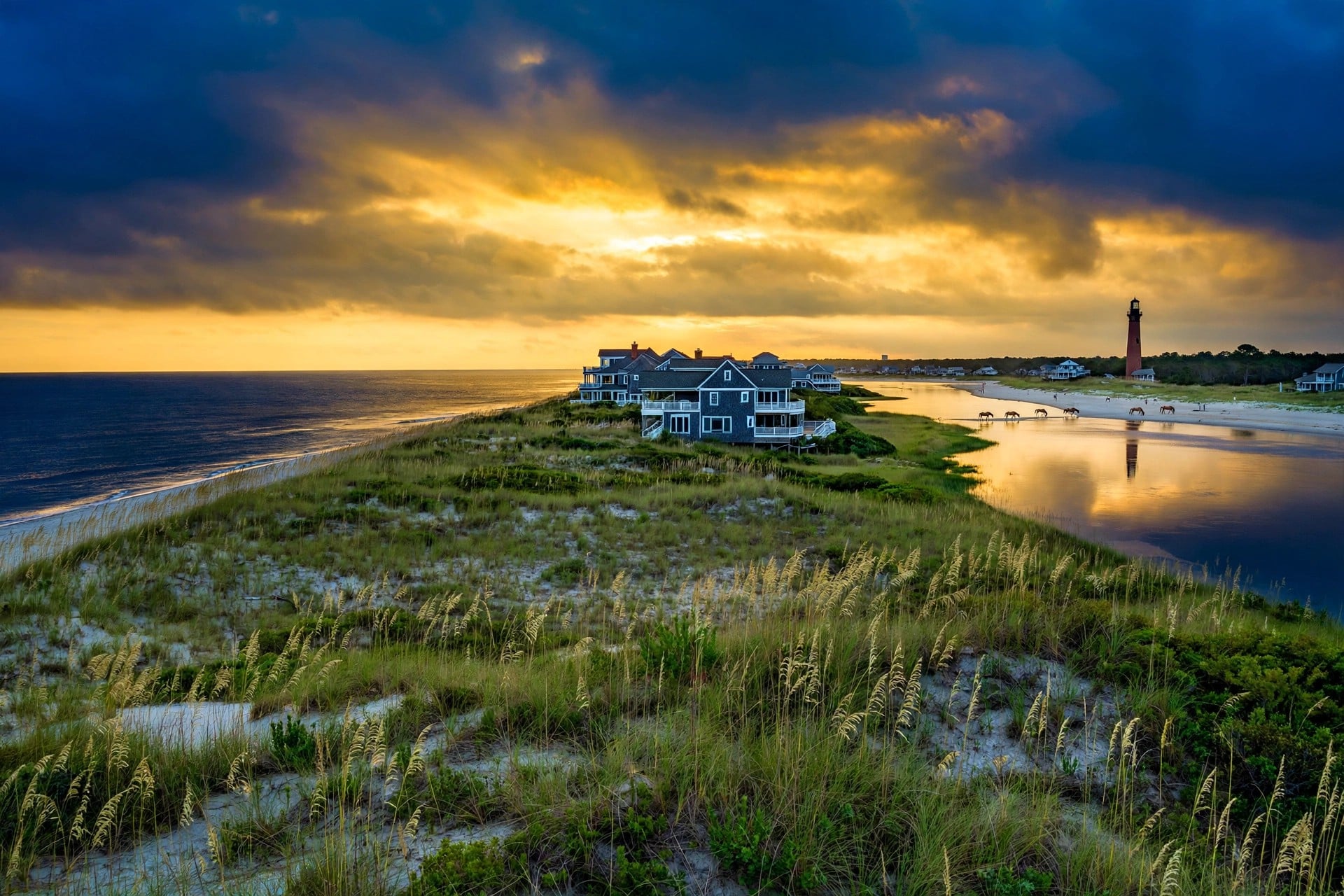 Corolla beach houses at golden hour with the Currituck Beach Lighthouse and wild horses on the beach