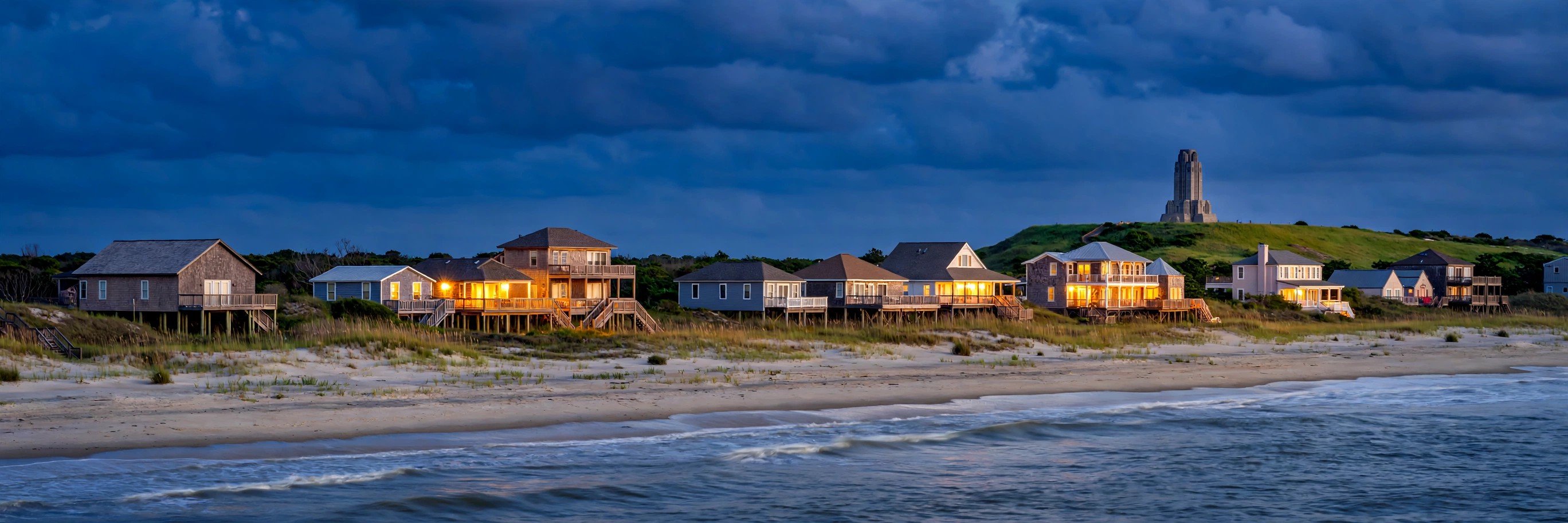 Kill Devil Hills beach houses at dusk with the Wright Brothers Memorial on the hill behind them