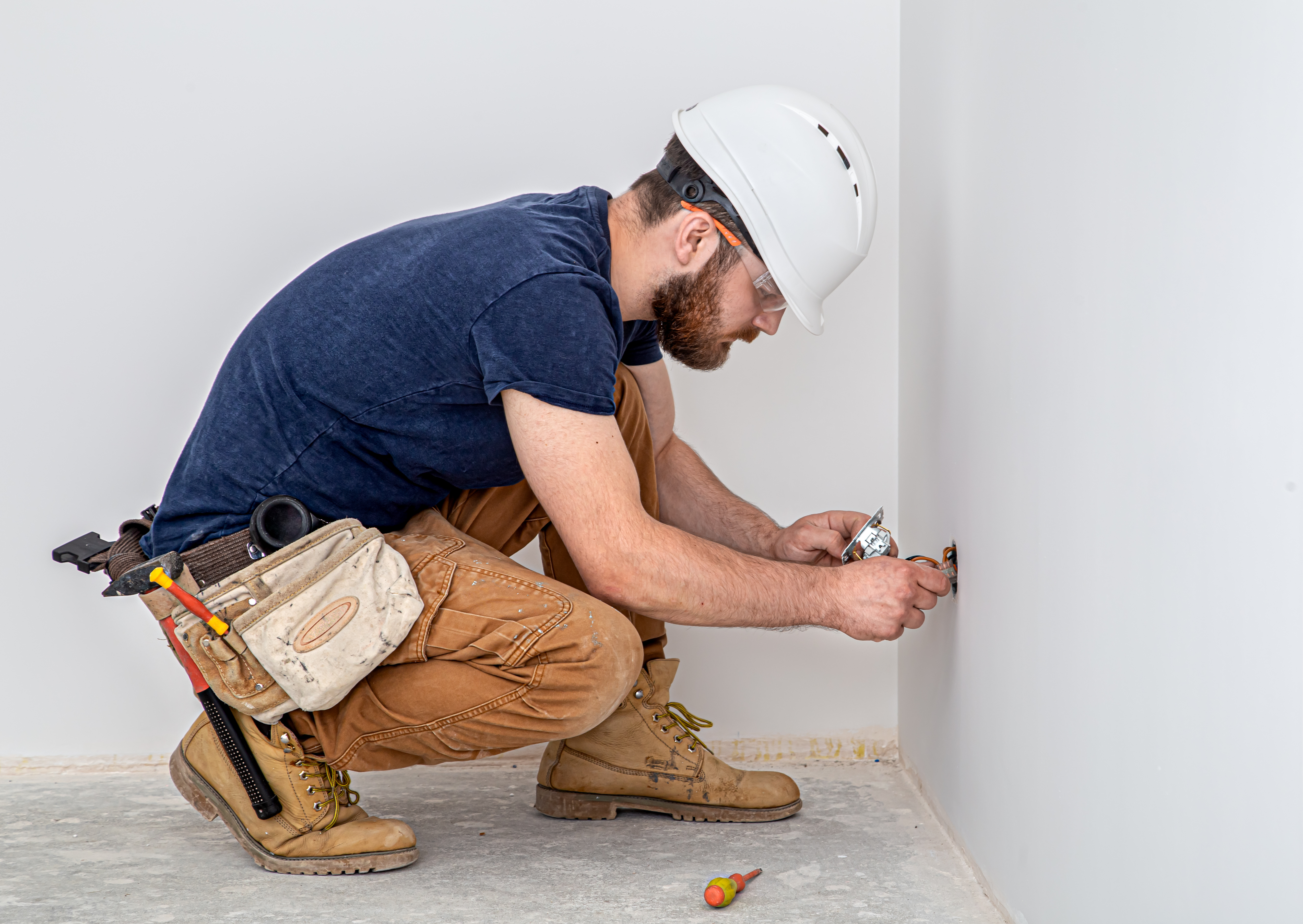 Electrician Builder at work, installation of sockets and switches. Professional in overalls with an electrician's tool. Against the background of the repair site.