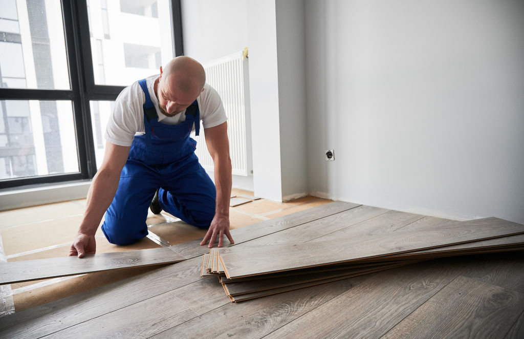 Man installing laminate timber floor in apartment under renovation.