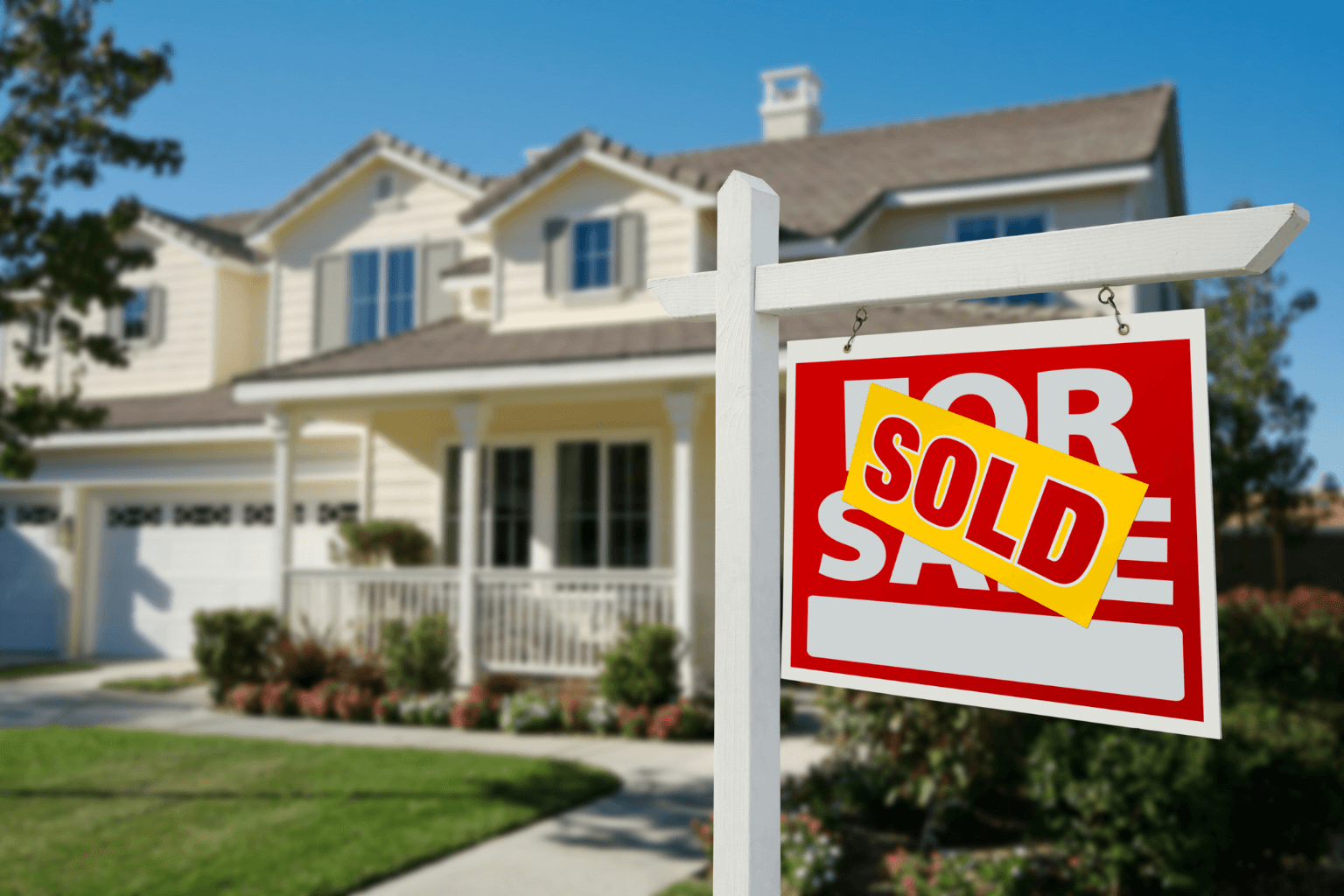 A “Sold” real estate sign in front of a house.