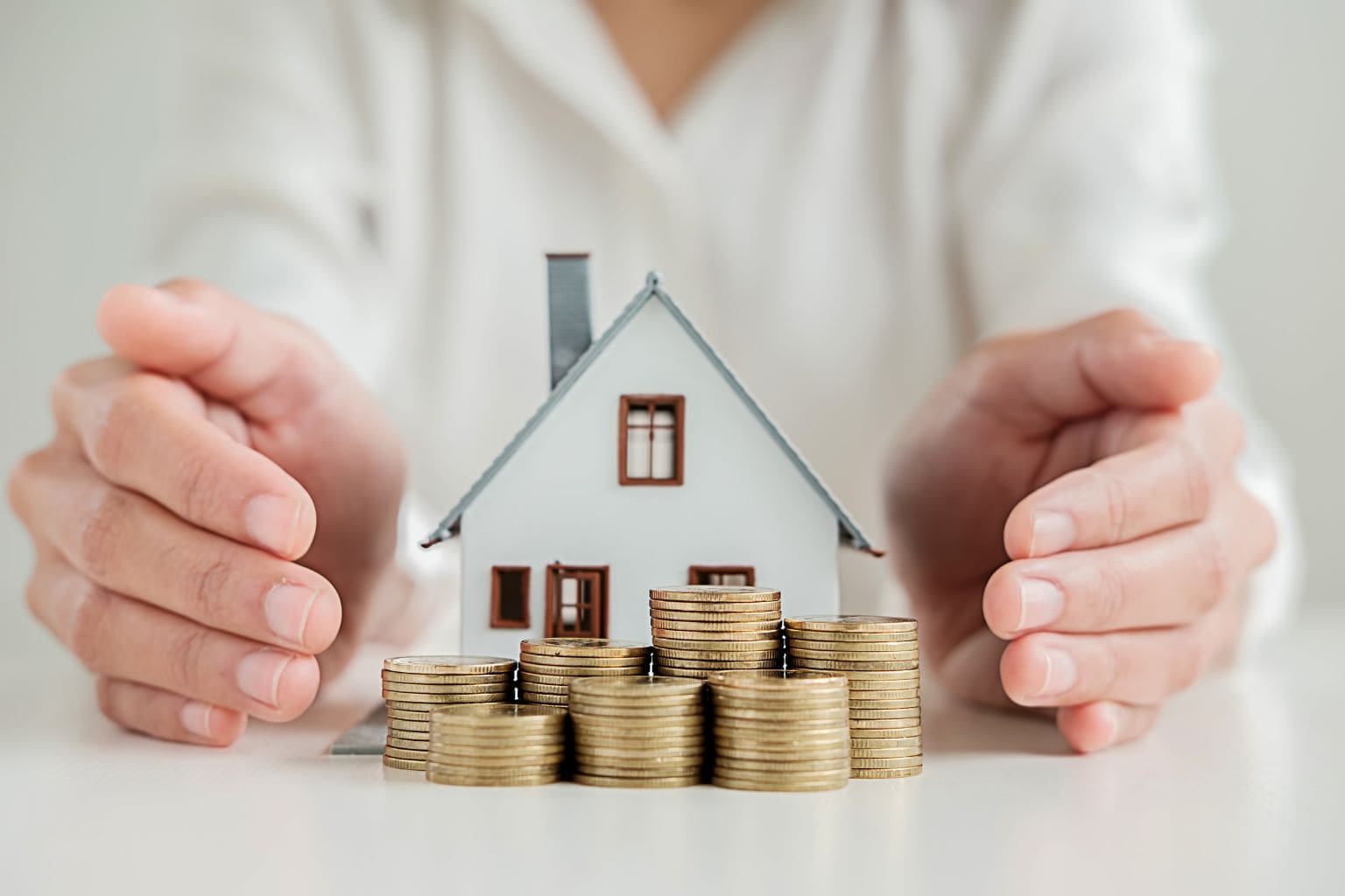 Creative Financing Tips for Buyers in Concord: Hands holding a small model house with coins around