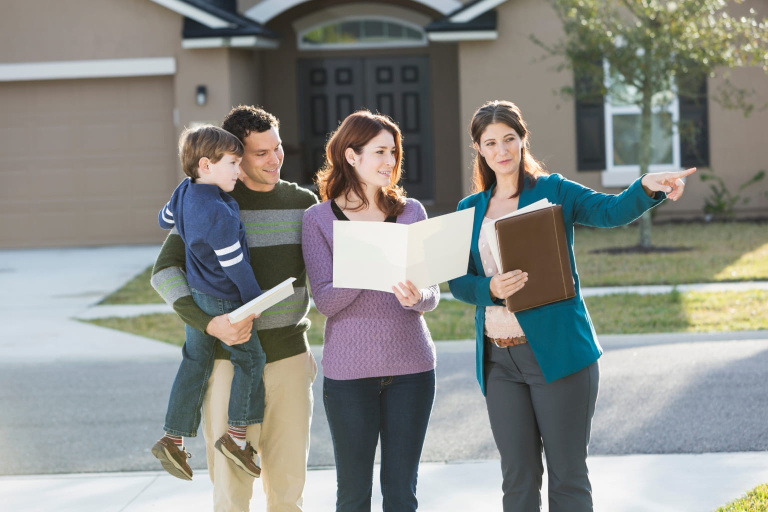 Real estate agent showing a home to buyers outside a house.