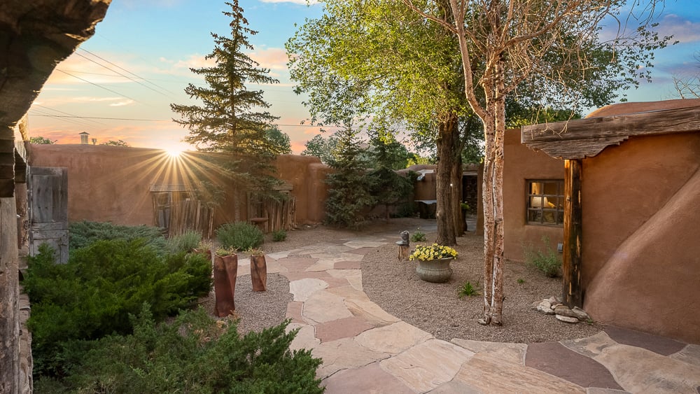 Sunset over an adobe courtyard with flagstone walkway, timber vigas, and native plantings in Taos, New Mexico.