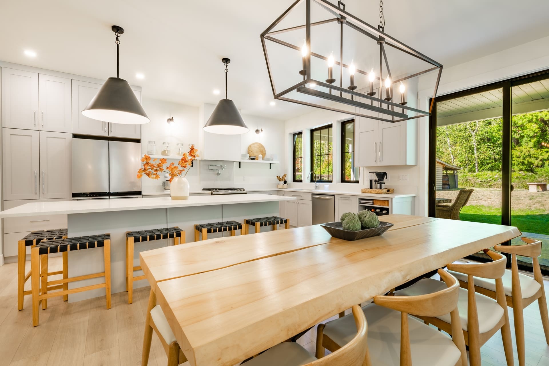 Modern farmhouse kitchen interior with light wood floors white granite marble counters large dining table with eight chairs stainless appliances orange