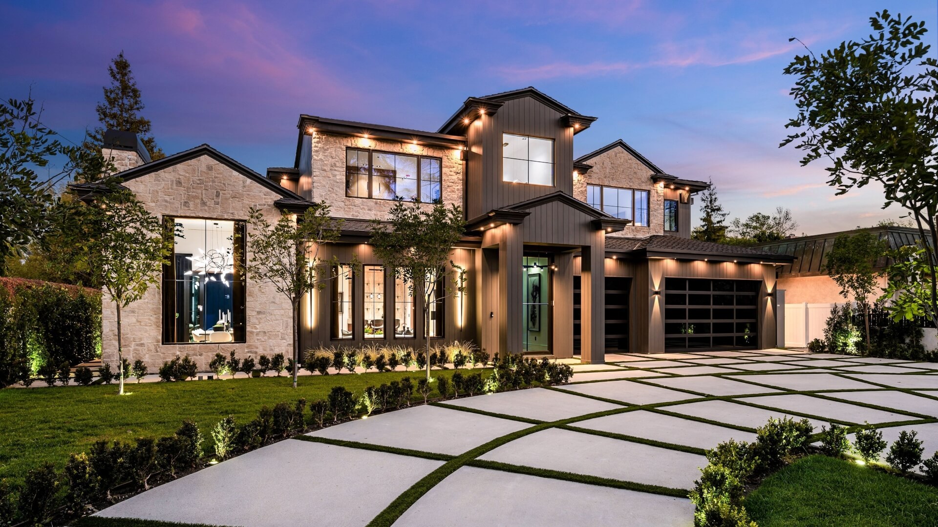 Modern luxury home exterior with a beautifully landscaped front yard and driveway at dusk
