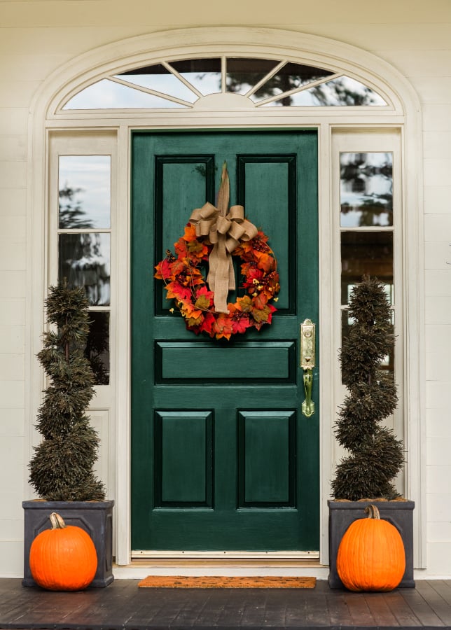 Green front door with fall autumn wreath with leaves and topiaries and pumpkins