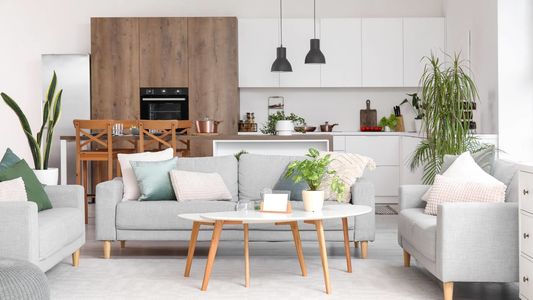 Interior of light open space kitchen with cozy grey sofas and coffee table