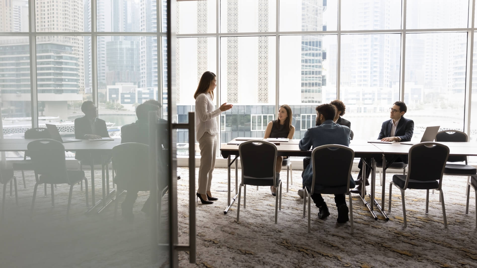 multiethnic business team, meeting, office conference room, brainstorming in co-working space with large window. Project leader woman talking to colleagues