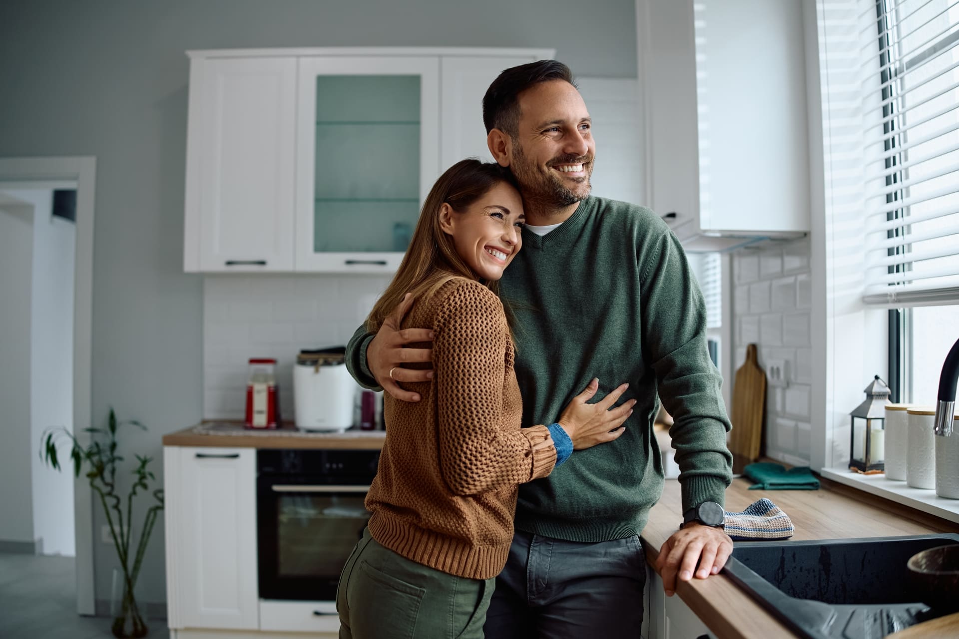 Embraced couple enjoying the view from their kitchen window. Copy space.