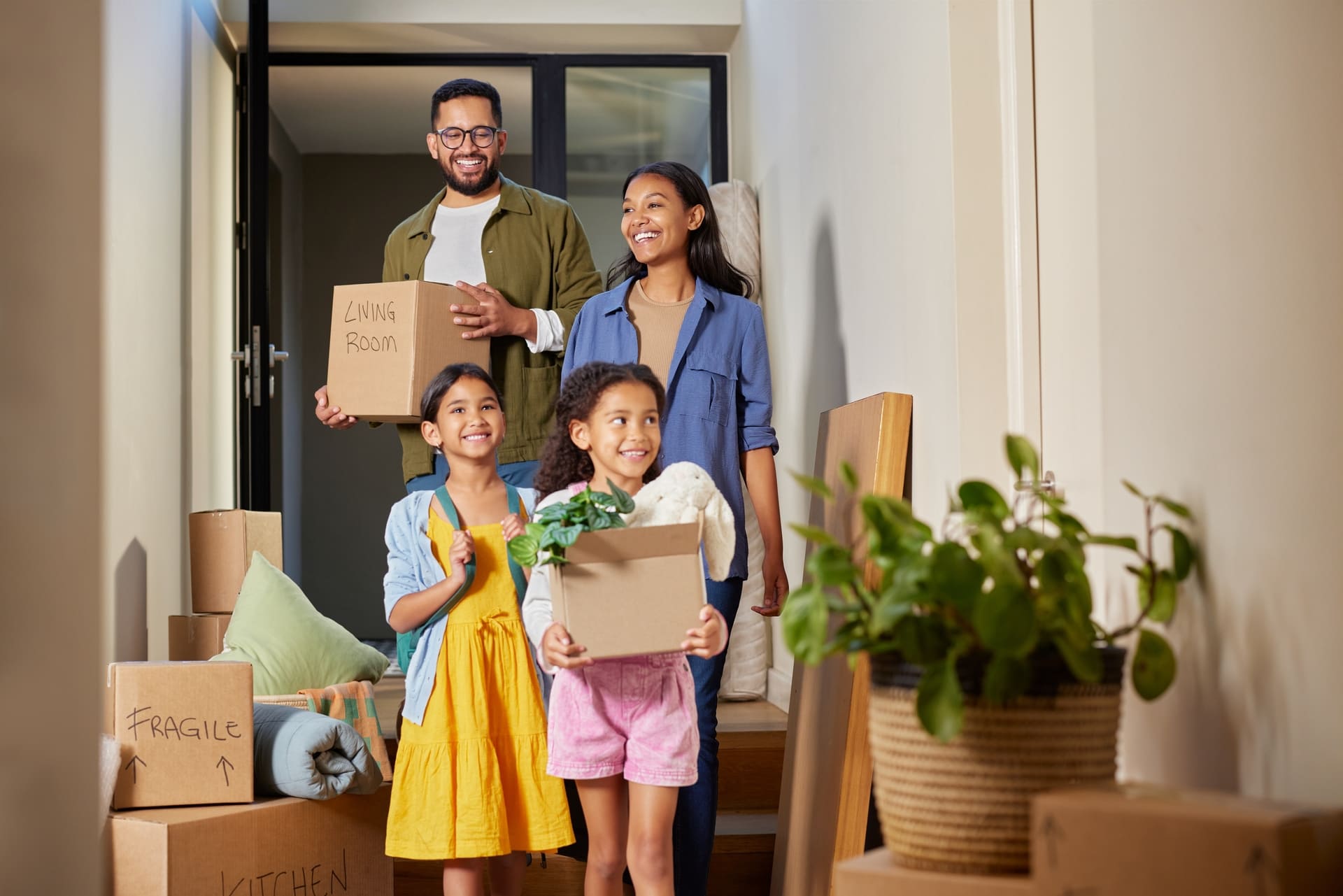 Happy mixed race family moving into a new home together. Middle eastern parents and children carrying boxes with smiles in new apartment. Happy smiling daughters helping parents on moving day.