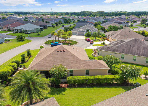 Aerial view of a quiet suburban neighborhood featuring single-story homes, palm trees, a circular cul-de-sac, and well-maintained green lawns under a sunny sky