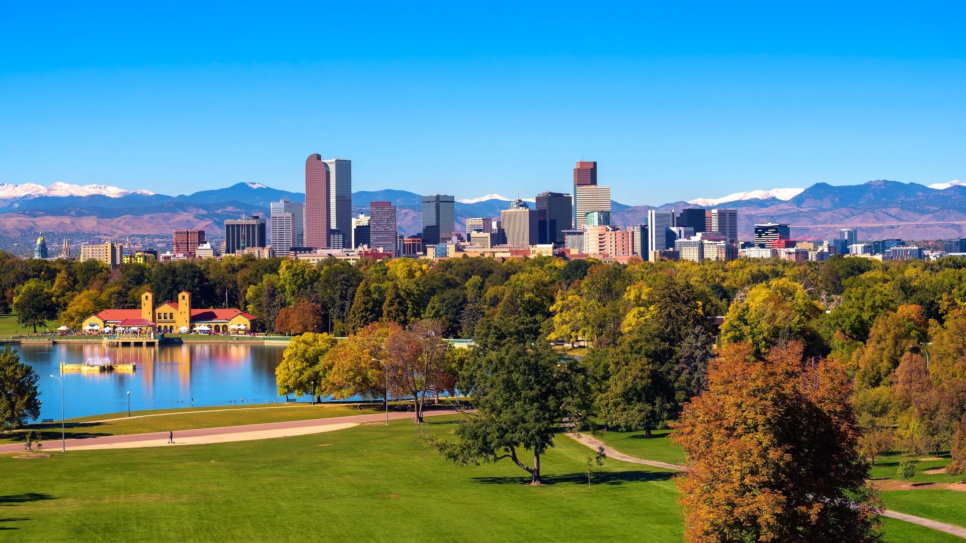 City skyline of Denver Colorado downtown with snowy Rocky Mountains and the City Park Lake.