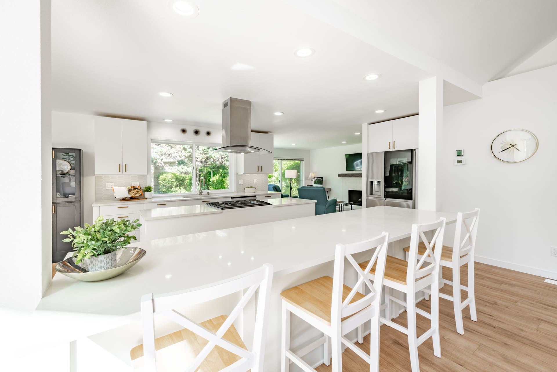 Bright white open concept kitchen with 2 island counters bar stools stainless appliances gold fixtures sink rang hood hardwood floor spacious