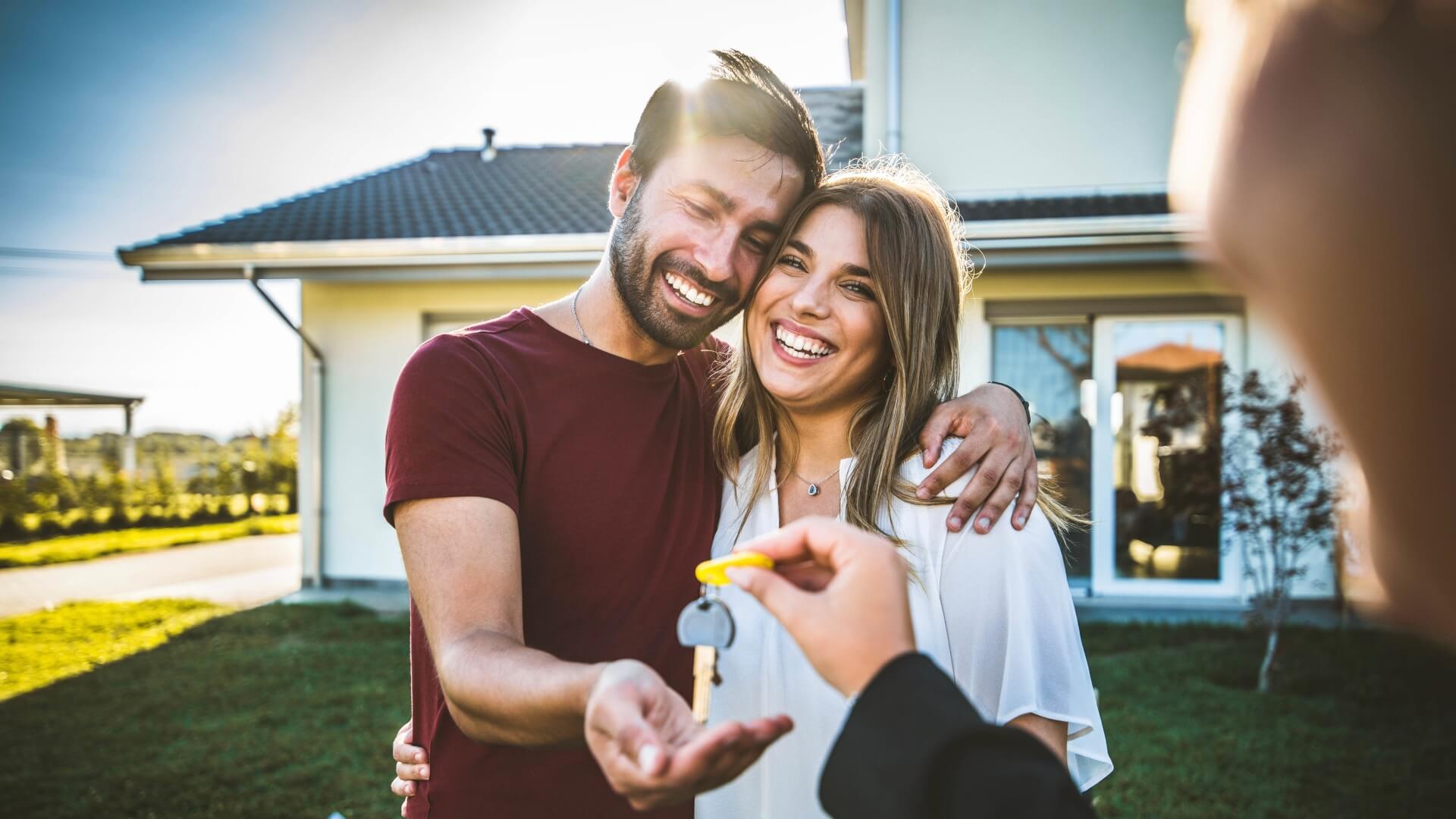 Happy millennial couple receiving keys from realtor, purchasing real estate - Family meeting with real estate agent - New house and real estate concept