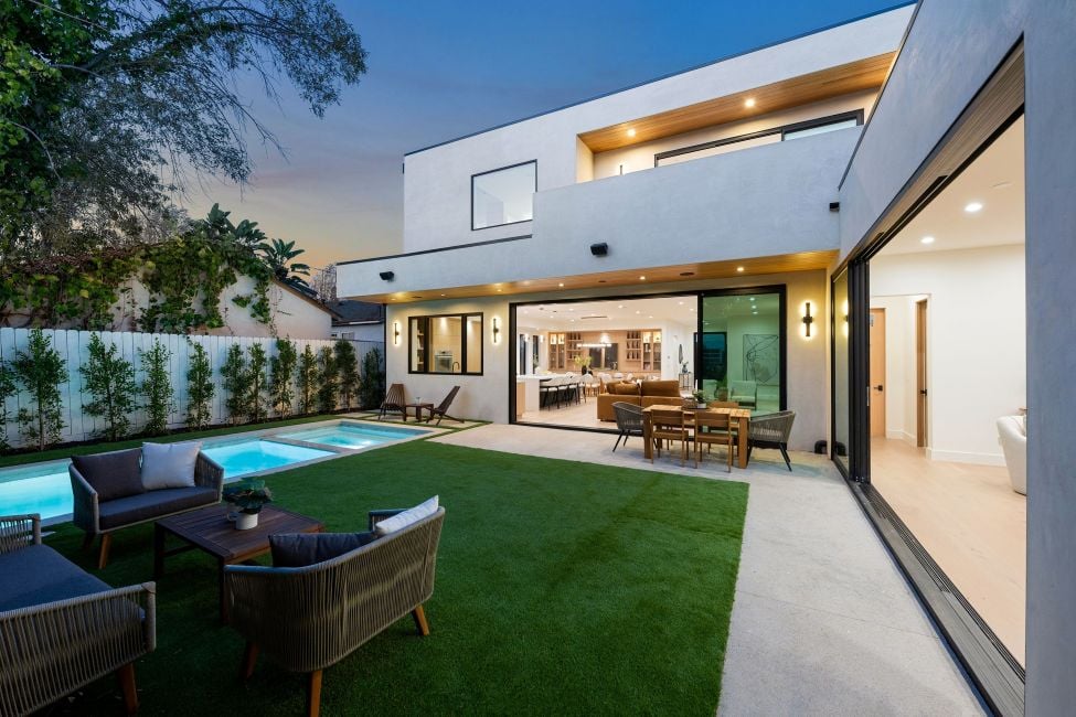 Modern luxury home with open living area, pool, and patio at dusk, featuring contemporary design and lush greenery. vertical