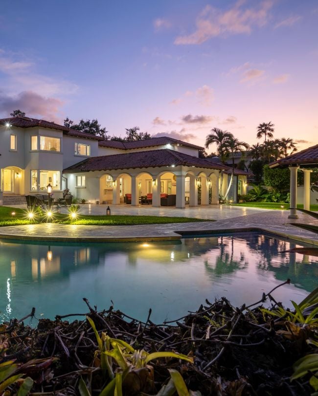 Florida, USA. January Backyard of a modern house with swimming pool, artificial grass, stone path, trees, chairs and an umbrella. vertical