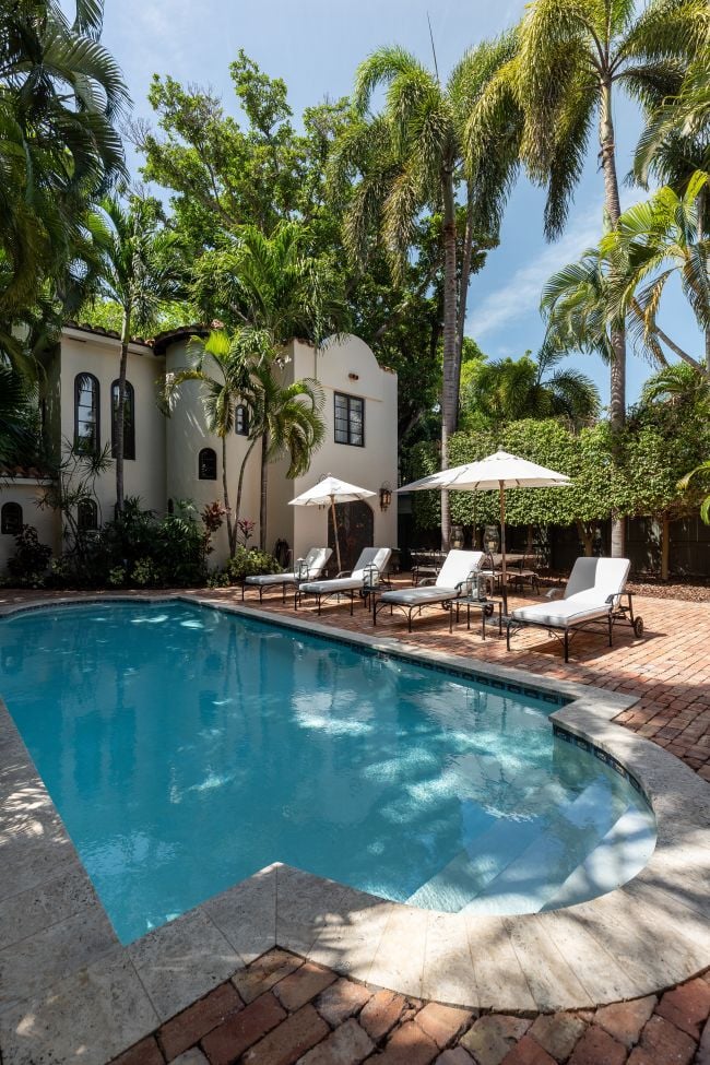 Florida, USA. January Backyard of a modern house with swimming pool, artificial grass, stone path, trees, chairs and an umbrella. vertical