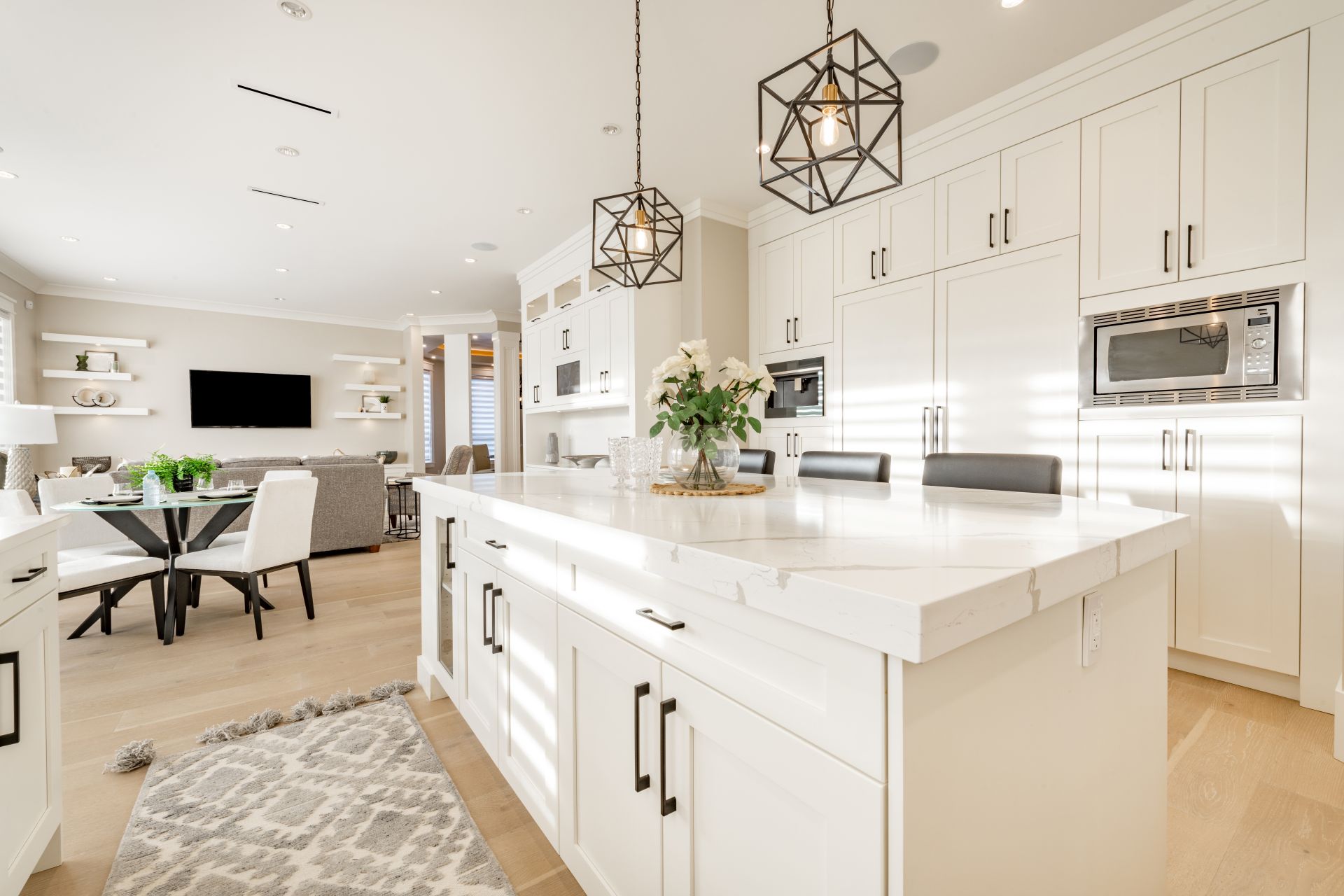 Warm white kitchen with expansive countertops island high end appliances spice kitchen black leather chair dining table wine fridge and office work station