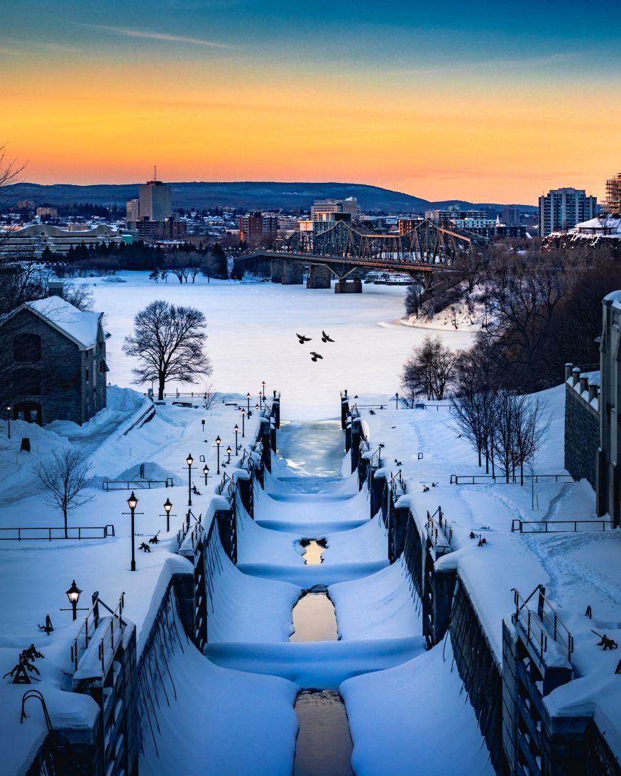 OTTAWA, CANADA - Rideau Canal Locks with beautiful winter sunset and birds flying by. Blue, yellow and orange sky with lots of snow on canal waterway
