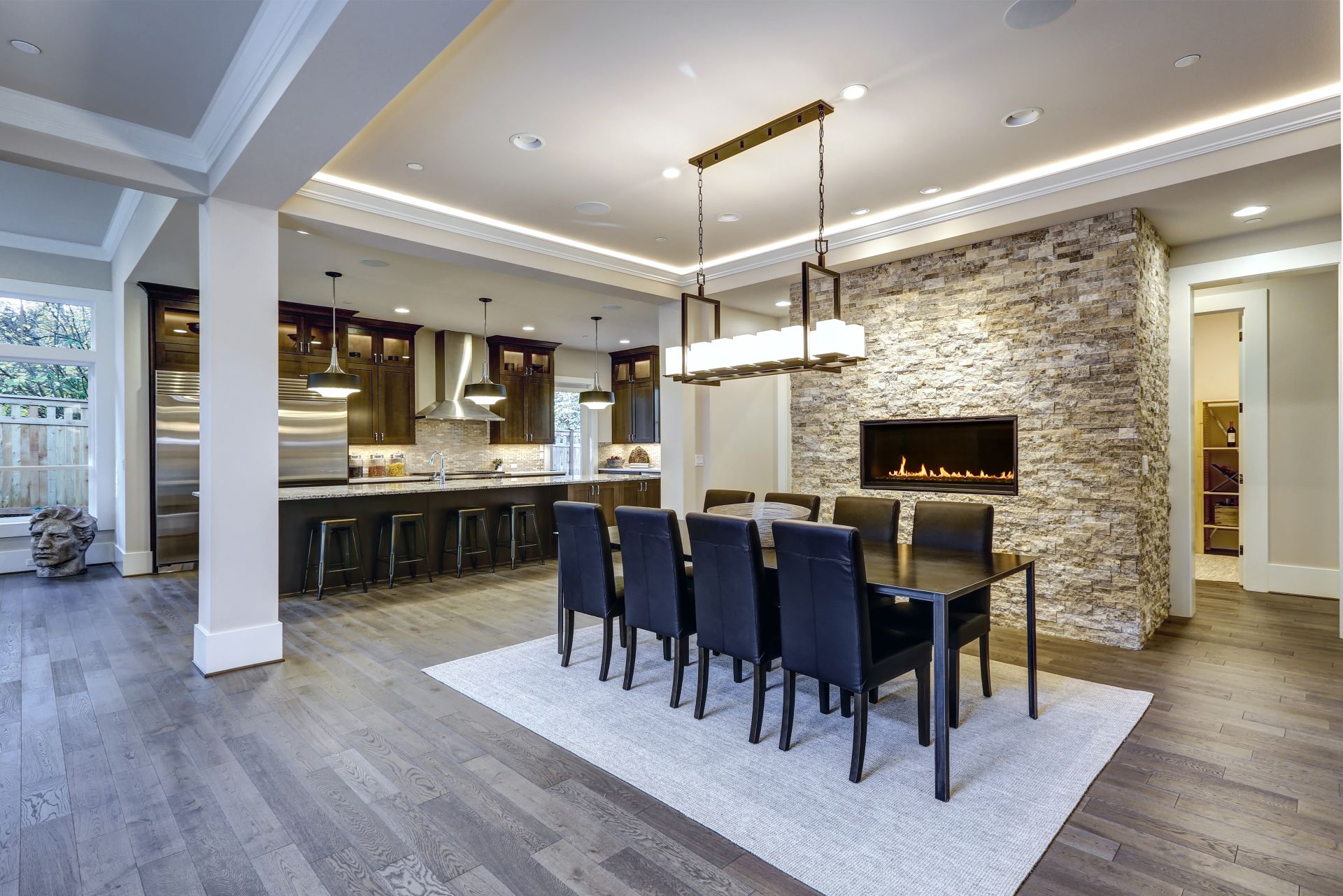 Modern open floor plan dining room design accented with stone fireplace wall facing black dining table lined with leather chairs and illuminated by rectangular chandelier. Northwest, USA
