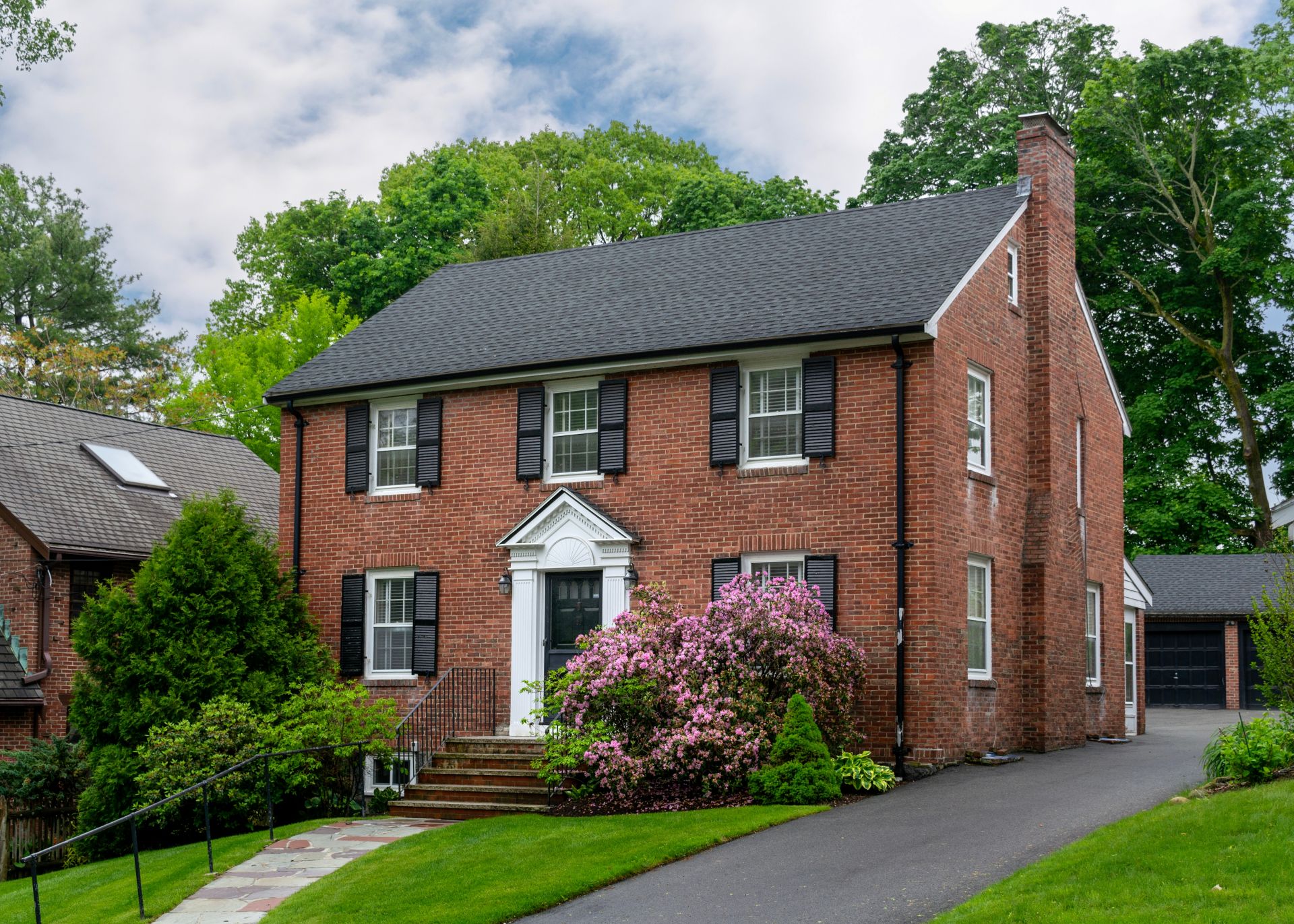 Beautiful two-story brick Colonial Revival house with black shutters and flowering bushes in Boston, Massachusetts, USA