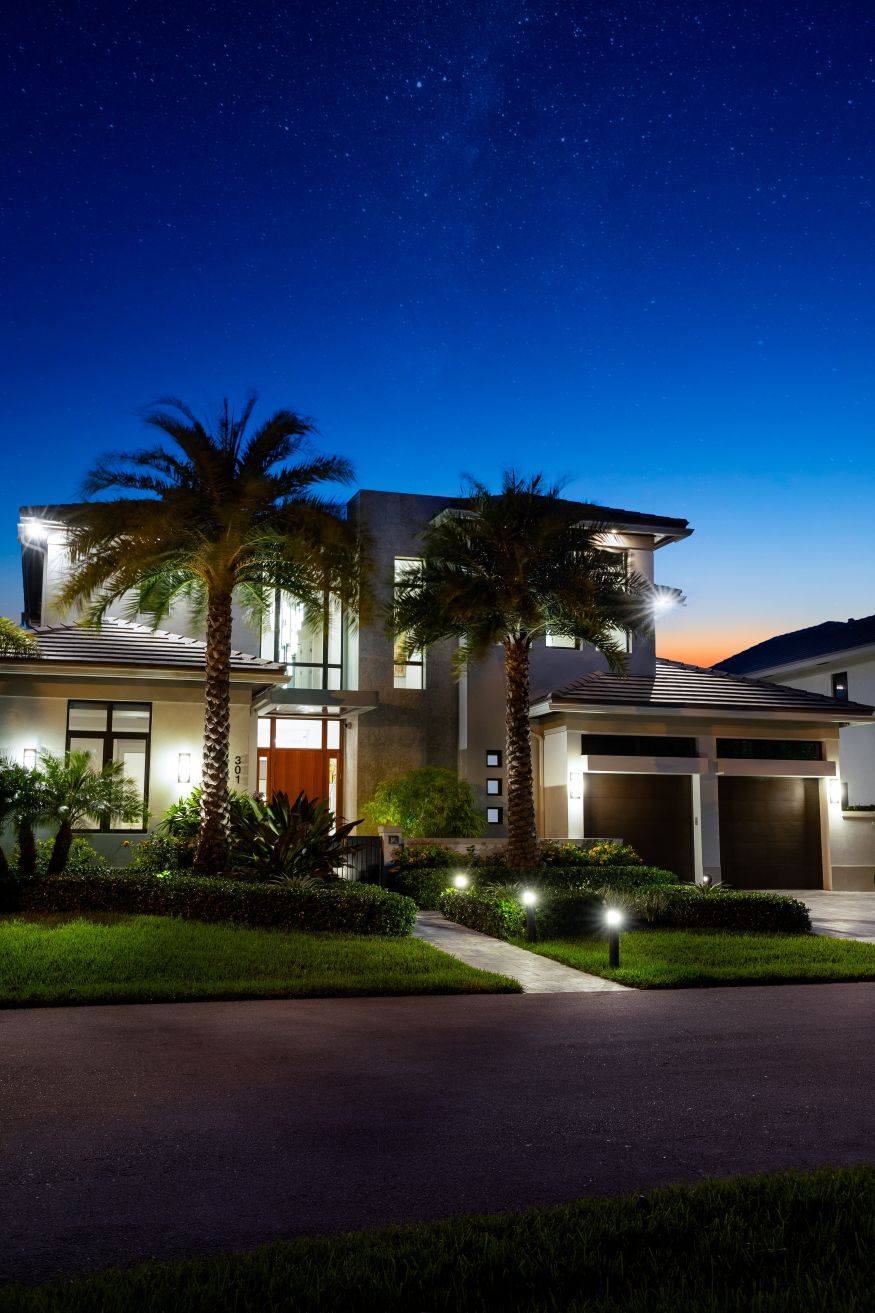 Contemporary Frontdoor Elegant Mansion Garden in Located in Florida, USA, showcasing modern architectural design, wooden furniture, beautiful green Vegetation, Blue Night sky Clouds.