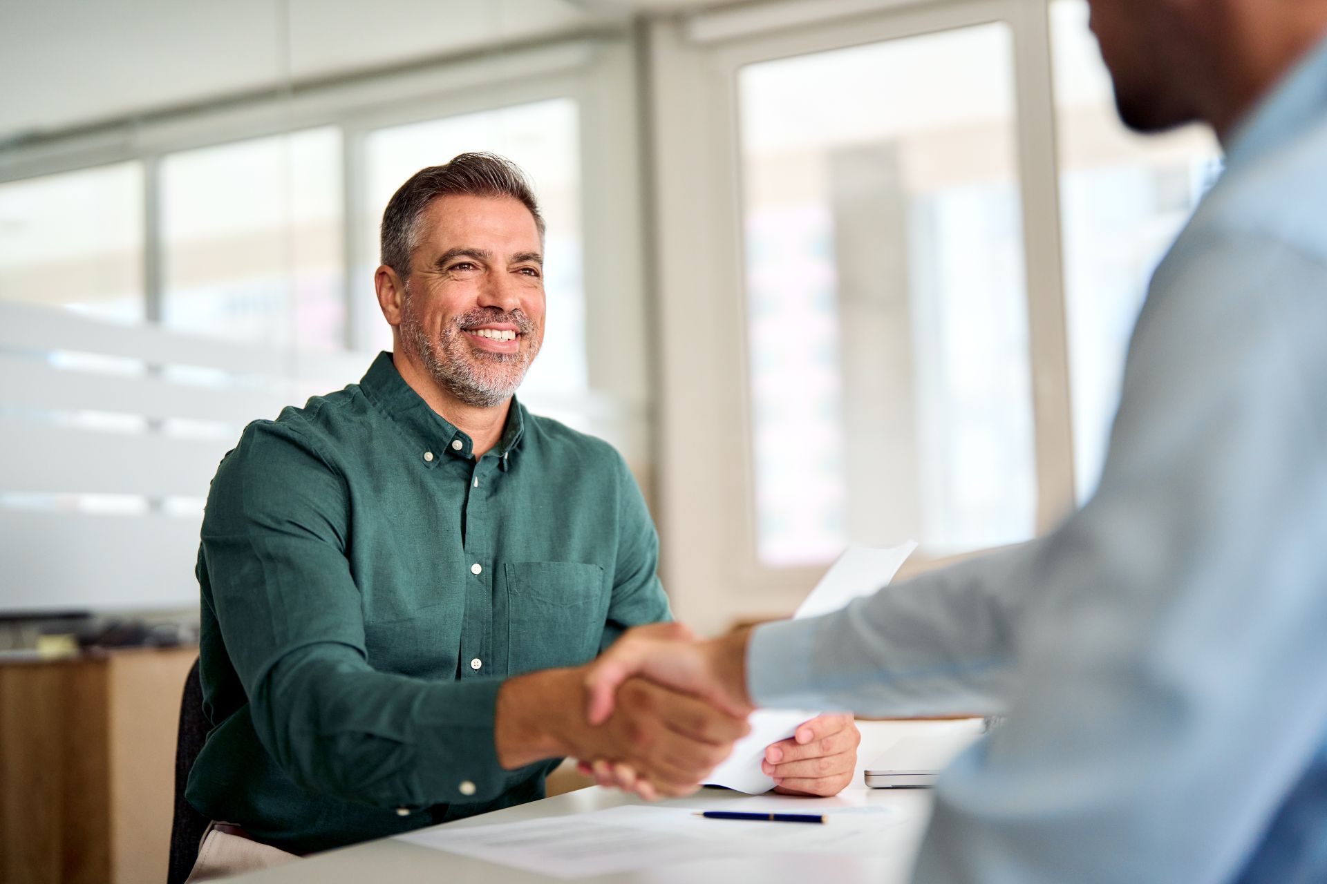 Smiling middle aged business man handshaking partner making partnership collaboration agreement at office meeting