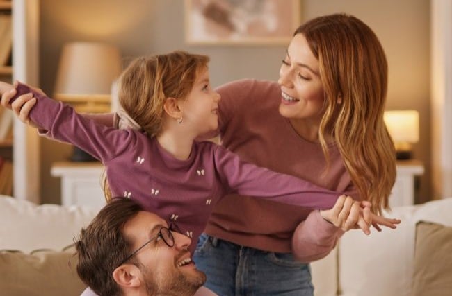 Mom, dad and little daughter playing flying game in the living room