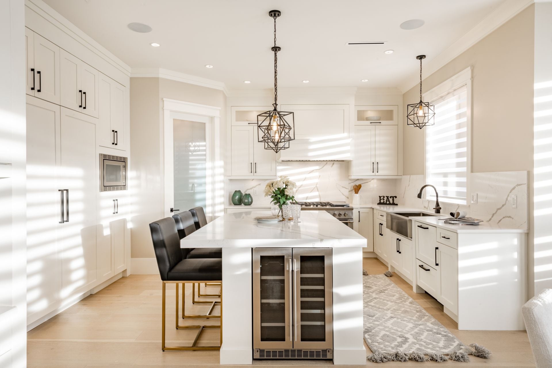 Warm white kitchen with expansive countertops island high end appliances spice kitchen black leather chair dining table wine fridge and office work station
