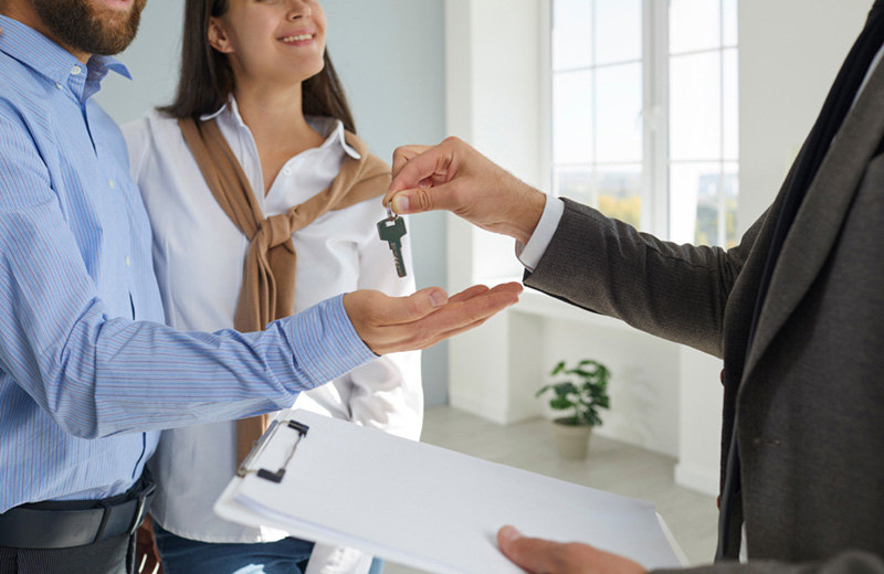 Real estate agent handing house keys to smiling first time homebuyer during closing meeting
