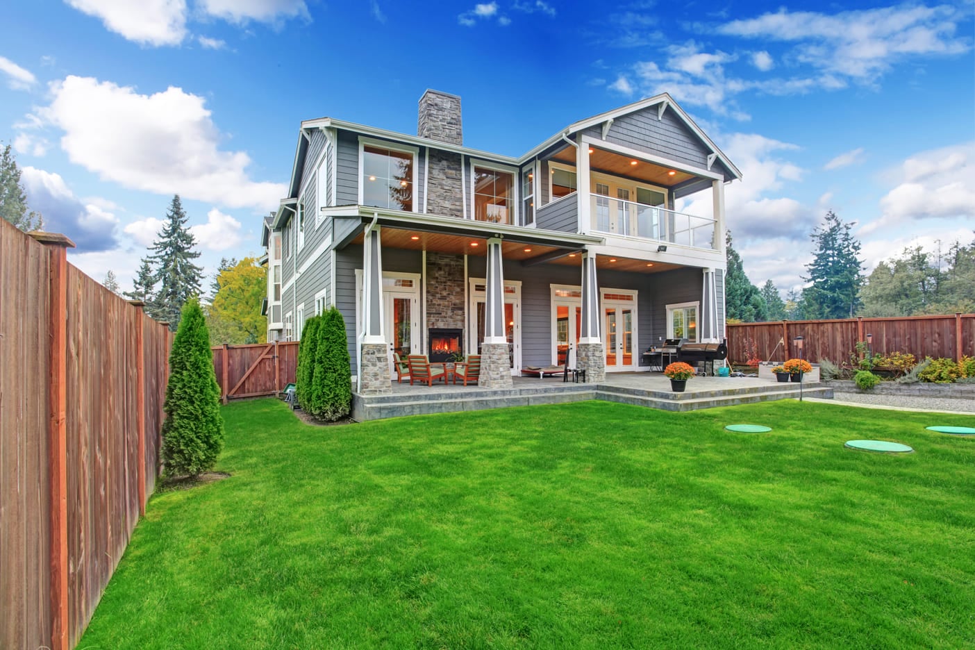 Luxury house with backyard walkout deck and column porch. View of lawn with trees and flower pots (2)