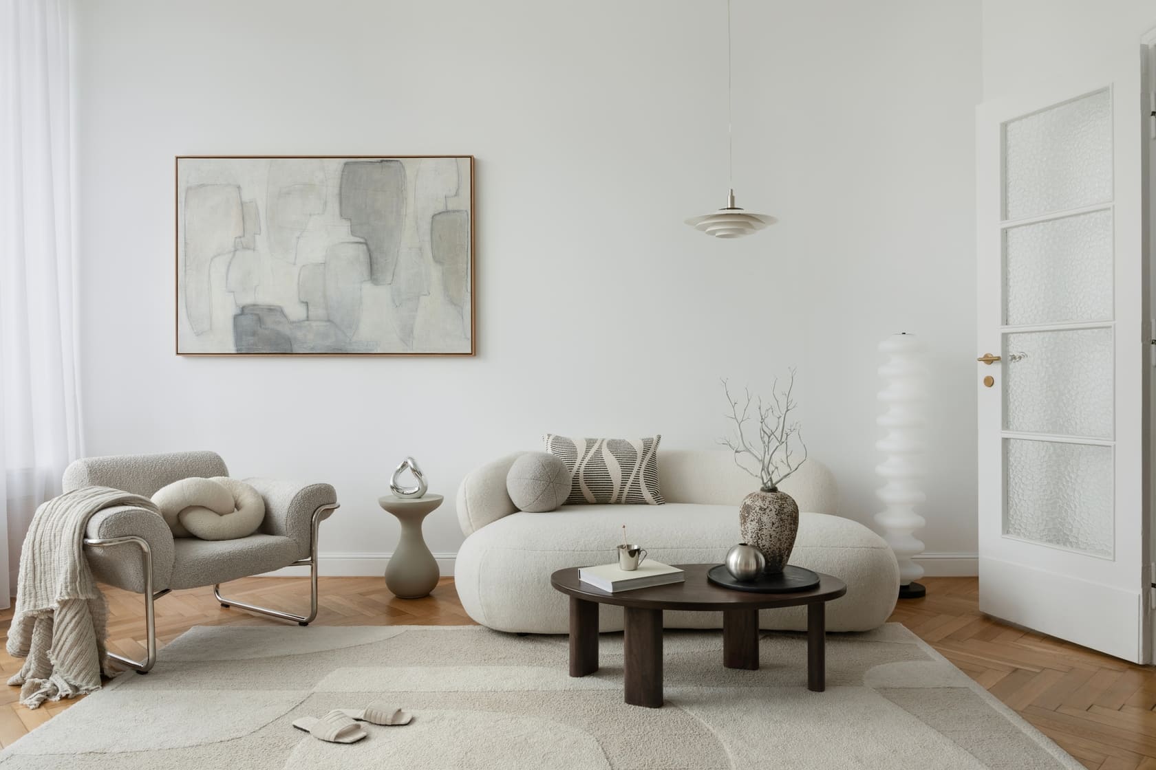 A serene living room with a neutral color palette, featuring a plush curved sofa, abstract artwork, and soft textures for a warm, modern aesthetic.